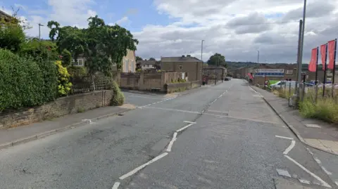 Google The junction of Westcliffe Road and the main road, Westgate, in Cleckheaton, with a blue, cloudy sky above.