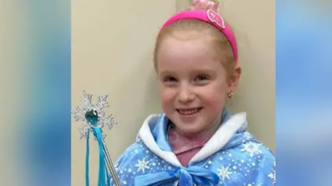 Family photo A young girl with red hair, wearing a pink headband and a blue cloak. 