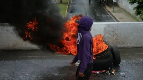 Jongeren van Reuters staan ​​naast een brandende band in Caracas