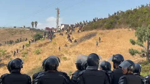 Moroccan security forces monitor dozens of migrants who have gathered on the outskirts of the border town of Castillejos, Morocco