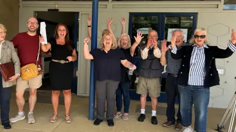 A group of residents celebrating outside Durham council HQ after a planning meeting. Some are clapping and have their hands in the air.