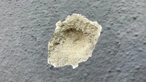 Shows a bullet strike on a grey wall