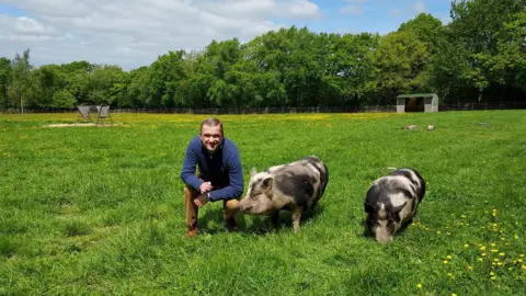 Ferne Animal Sanctuary Kevan Hodges kneeling down beside two pigs in a field