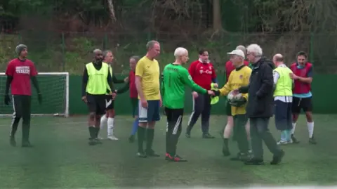 A group of players after the match. Gottesman in yellow shakes hands with the oppositions goalie who is dressed in green. 