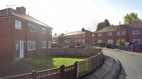 Google A street with houses lined on either side, there is a bend in the road and the houses are red brick semi-detached