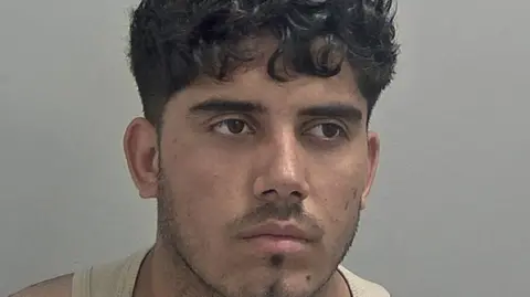 Warwickshire Police Mugshot of Ahmed Mulakhil, wearing a beige vest.