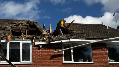 Two houses have a large hole in the roof - a man is standing in the gap