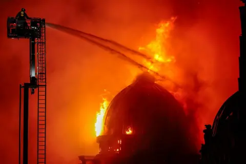 Getty Images Huge fire with dome burning. The whole sky is orange and fire fighters are spraying water on the building