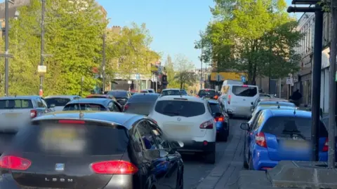 Lots of cars parked in both the middle of a road and the neighbouring lay-by.