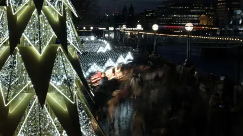 Reuters People walk across the Winter by the River Christmas market near Tower Bridge, in London