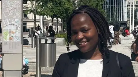 Greater Manchester Police Barbara Nomakhosi smiling in the sunshine in a smart black jacket and white top.