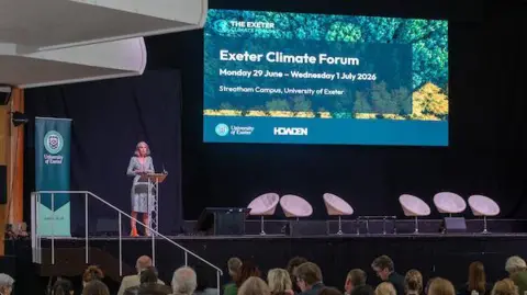 University of Exeter A woman stands on stage at the Exeter Climate Forum at the University of Exeter 
