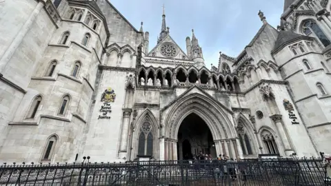 A large gothic court building with black railings out front, white stone walls, arched and vaulted windows and turrets and towers.