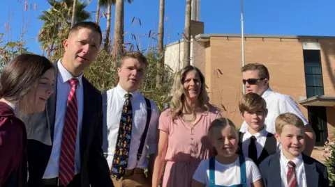 Spencer Taylor A man and woman standing outside a church with their six children. They are all smartly dressed.