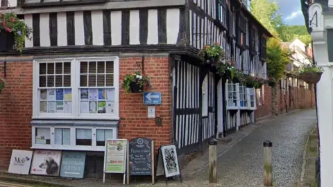 Google A historic street in Ledbury. There are signs for boutique shops and a narrow alleyway.