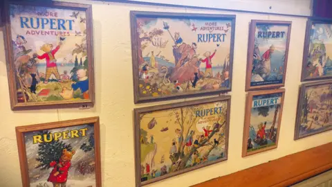 Simon Furber/BBC A wall featuring cartoon illustrations of a bear named Rupert. 