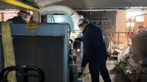 Ukrainian Action Two engineers work on the inside of the generator. They are in a warehouse. 
