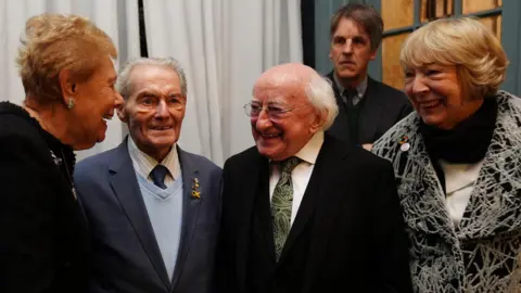 PA Media Four people all smiling and greeting each other. Michael D Higgins is wearing a black suit jacket, white shirt and green tie. 