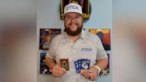 Nick Jarman Nick Jarman wearing a polo top and holding Pokémon cards