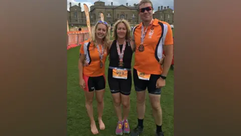 Family photo Jane Blackwell is wearing black running gear with a competitor's lanyard around her neck. She has her arms around her two children, who are also in running gear.