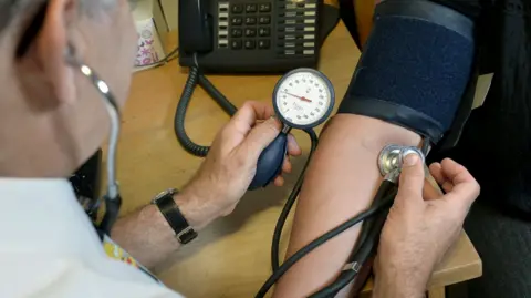 PA Media A doctor tests the blood pressure of a person whose arm can be seen.