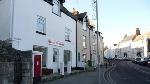 Chris Downer / Geograph An old photo of the post office in Reforne, Easton. There is a red wall post box outside the whitewashed terraced building. The rest of the houses in the street are grey or bare stone.