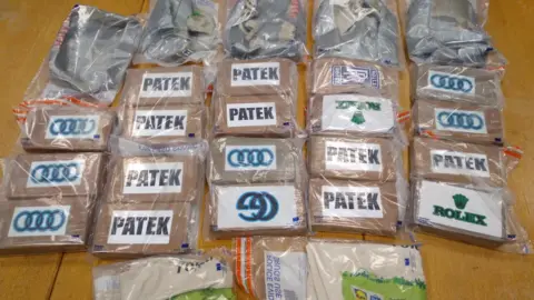 Essex Police Nineteen brown boxes containing drugs, all sealed up in evidence bags. They are laid out on the floor and each have the names of luxury brands on them, including Audi, Rolex and Patek Philippe