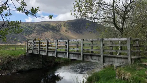 River Caldew with Carrock Fell in the background. A wooden bridge goes over the water.