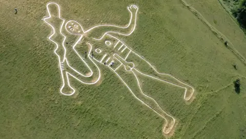 BBC/Kevin Church A chalk figure on a grassy hill shows a 55m naked, club-wielding man