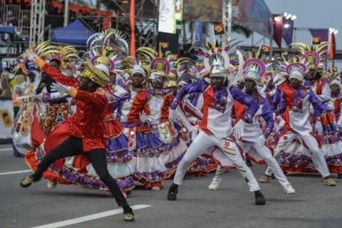 Julio Pacheco Ntela / AFP A Drum Major memimpin prosesi pria dan wanita yang mengenakan pagentry ungu, merah dan putih. Mereka semua menari tarian latar dalam waktu.