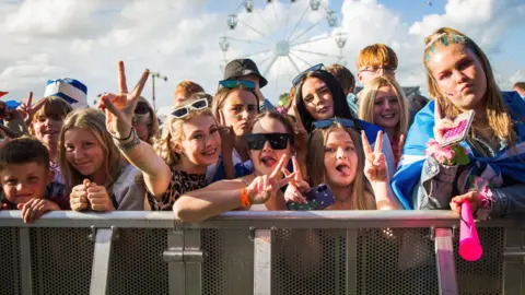 Dumfries and Galloway Council A crowd of young people behind a barrier at a sunny outdoor music festival.