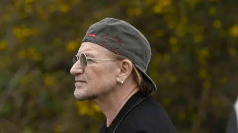 PA Shows Bono with baseball cap back to front and wearing glasses