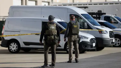 Two FBI agents outside stand outside Georgia election facility. They're wearing ballistic vests marked "FBI" and are standing in front of yellow caution tape.