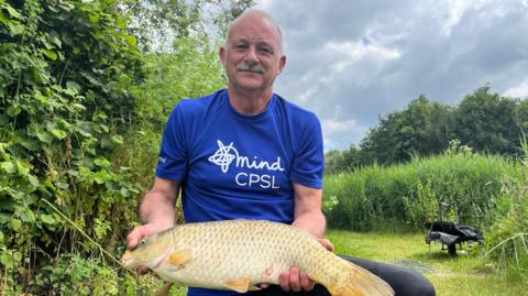 Ian Darler wearing a blue top which reads Mind CPSL while holding a fish