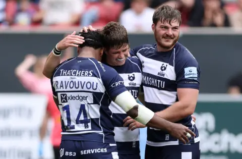 Three Bristol Rugby players celebrate scoring a try against Harlequins at Ashton Gate