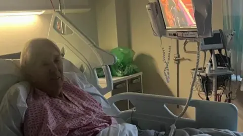 Nikki Zilli Maureen is in a hospital bed, wearing pink nightwear