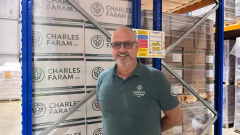A man wearing glasses and a T-shirt reading "Charles Faram" with a logo on the top right stands in front of boxes with the same brand logo.