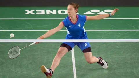 PA Media Kirsty Gilmour, wearing her blue Commonwealth Games outfit, lunges forward to try and reach the shuttlecock during a 2014 match at the Games in Glasgow