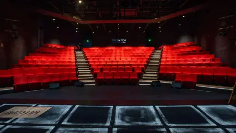 A large theatre with red seats in rows.