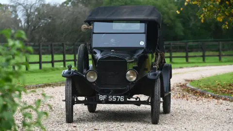 Historic Auctioneers A black 1925 Ford Model T two-seat runabout being driven along a windy shingle driveway in the countryside 