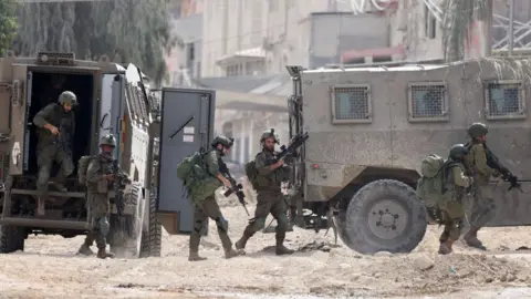 AFP Five soldiers carry heavy weapons as they walk alongside two vehicles with rubble underneath their feet.