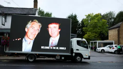  "Welcome to the UK, Donald." The van is pictured in a small car park with a few white cars parked at the side, under an overcast sky.