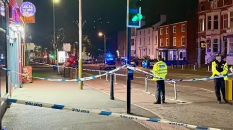 Police tape across traffic lights with two police officers at the scene on London Road in Leicester.