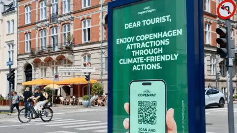 Adrienne Murray Nielsen An advert for CopenPay is in the foreground of a street in Copenhagen with a cyclist on it