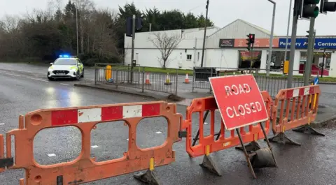A road closed sign and a police car with a garage in the background
