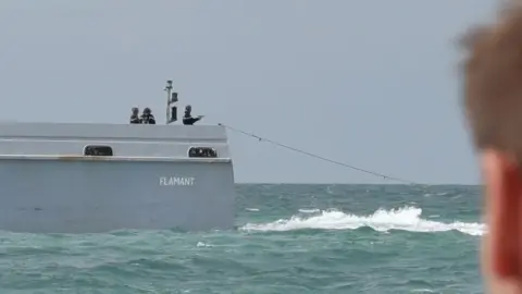 A French patrol officer at the back of the boat pointing a pistol towards the sea