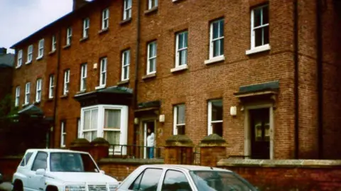 ROUNDABOUT A row of red-brick three-storey terraced properties. A woman is at the doorway on Roundabout's old base in the 1970s.