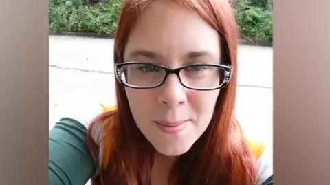Aimee Betro wearing a Green Bay Packers T-shirt. She has red hair and black-framed glasses