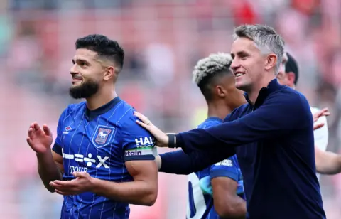 Getty Images Ipswich Town Manager Kieran McKenna playfully pushes Sam Morsy towards the away fans of Ipswich to receive his applause following a goal. Morsy, in his full Ipswich Town kit, and wearing the Premier League captain's armband applauds the away support.