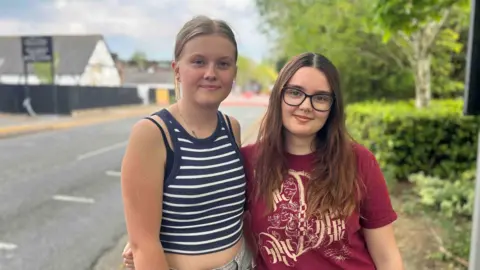 Kate Bradbrook/BBC Two young girls stand with their arms around each other on a residential street